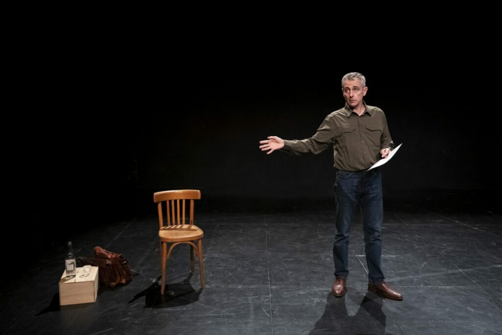 Homme sur scène tenant une feuille et faisant un geste de la main